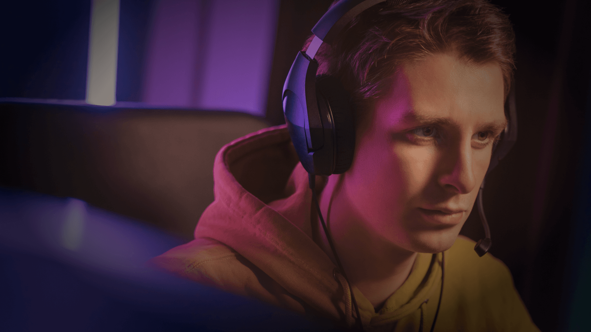 Young Man with headphones looking intensely at a screen waring a yellow hoodie